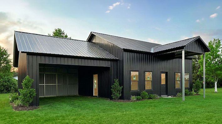All-black modern steel barndominium with split roofline and open side porch
